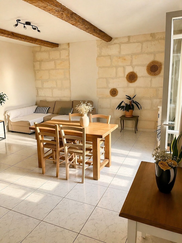 A dining area with a wooden table and chairs, a sofa, and a stone wall.