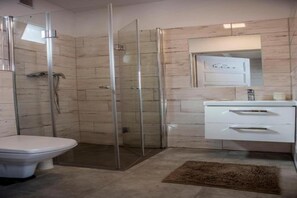 Een badkamer met een douche met glazen wand, toilet en een wastafel met lades.
