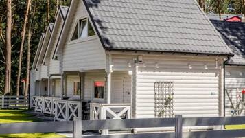 Eine weiße Blockhütte mit geneigtem Dach, einer Veranda mit Geländer und einem eingezäunten Garten.