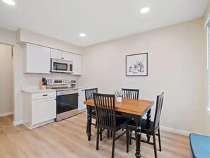 Een moderne keuken met witte kasten, een magnetron, een oven en een eettafel met vier stoelen.