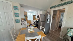 Una cocina compacta con muebles blancos, un refrigerador de acero inoxidable y una mesa de comedor con sillas blancas.