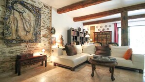 A living room with a stone wall, a white sofa, a glass coffee table, and a bookshelf. - Bastide nestled in the heart of nature (La Garde-Freinet)