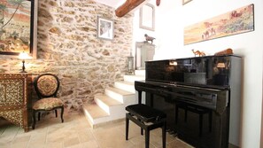 Ein Zimmer mit Steinwand, einem Klavier, einem Sessel und einer Treppe.
