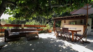 Eine Terrasse im Freien mit Holztisch und -stühlen, einer Holzbank und einer Pergola, die Schatten spendet.