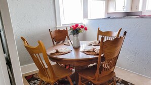 Ein Essbereich mit einem runden Holztisch, vier Holzstühlen, einer Vase mit roten Blumen und einem gemusterten Teppich.