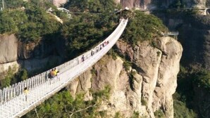 Un pont suspendu sur lequel des personnes se promènent, entouré de falaises rocheuses et de verdure.