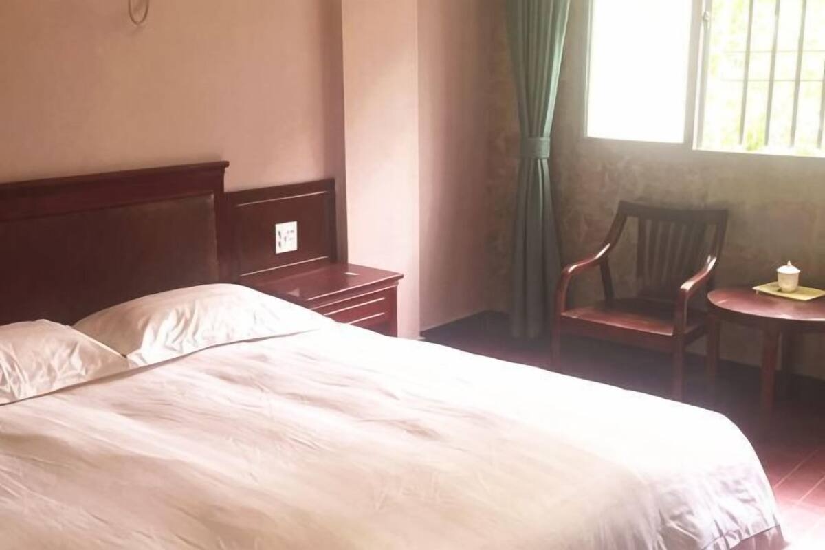 Una habitación de hotel con una cama, una mesita de noche de madera, una silla y una pequeña mesa con una lámpara.