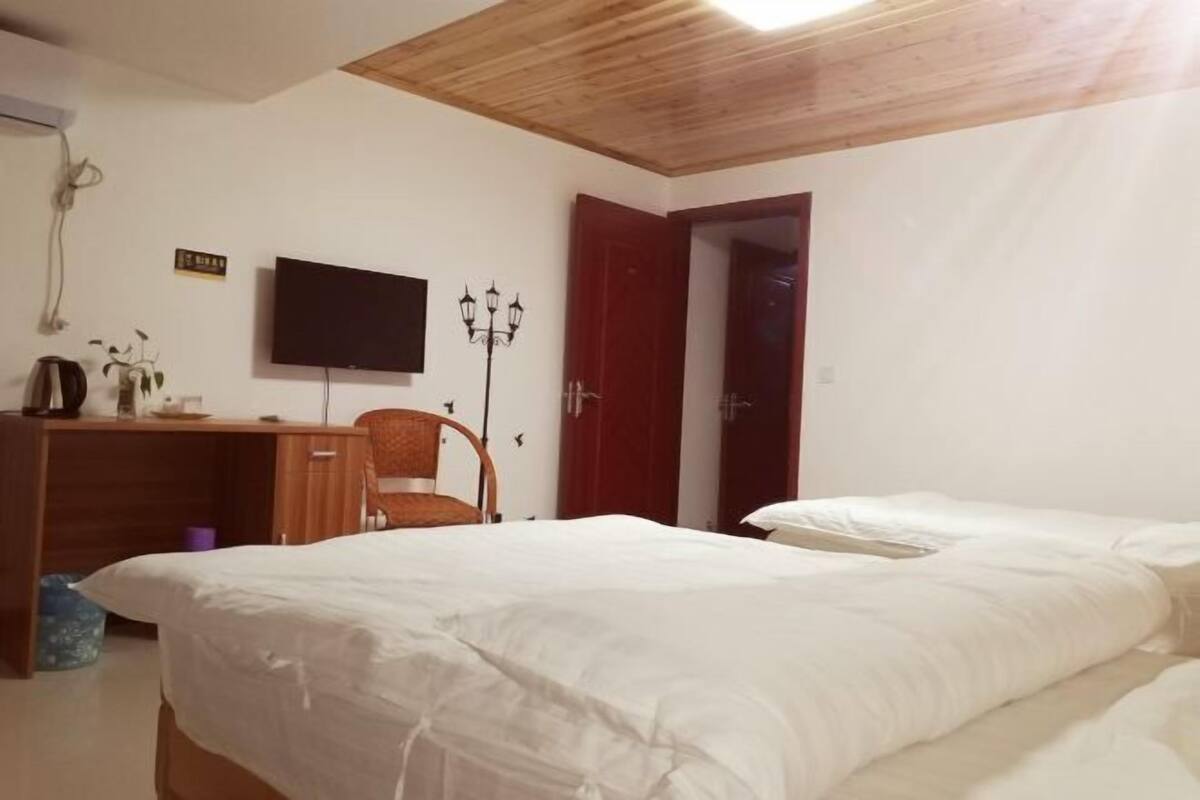 Un dormitorio con techo de madera, un escritorio con silla, un televisor y una cama con dos almohadas.