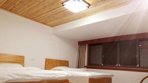 Une pièce avec deux lits en bois, une grande fenêtre avec des rideaux et un plafond en bois.