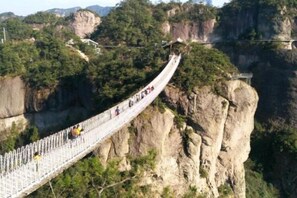 Un pont suspendu sur lequel des personnes se promènent, entouré de falaises et de verdure.