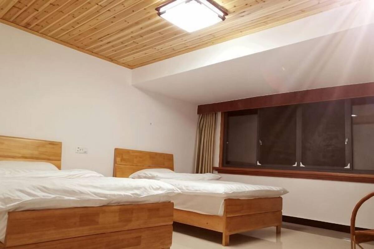 Un dormitorio con dos camas de madera, un ventanal con cortinas y techo de madera.