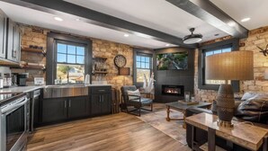 A modern kitchen with dark cabinets and a stone accent wall, a cozy seating area with a fireplace, and a large window overlooking a scenic view. - Modern Rustic Loft Suite in Downtown Blue Ridge (Blue Ridge)