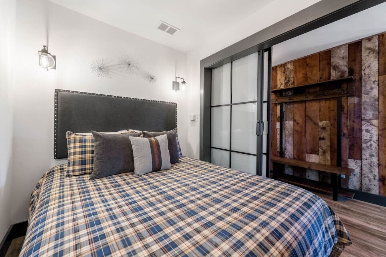Quarto com cama, cabeceira, luminária fixada na parede e armário de madeira.
