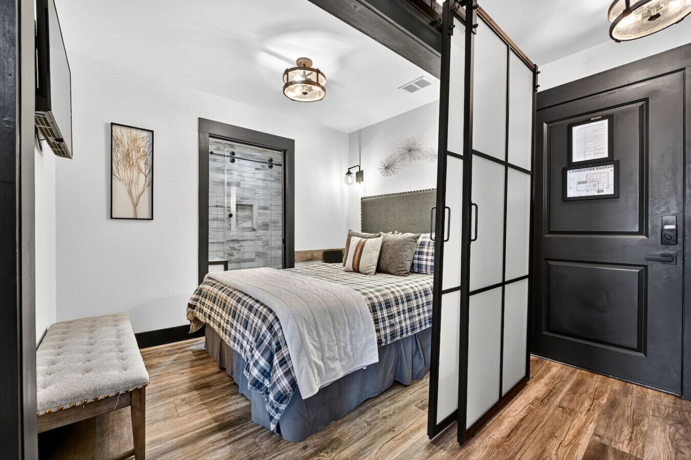 Een slaapkamer met een bed, een bankje, een garderobe en een deur met een bordje.