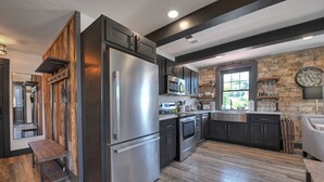 A modern kitchen with a stainless steel refrigerator, dark cabinetry, and a stone accent wall. - Modern Rustic Loft Suite in Downtown Blue Ridge (Blue Ridge)