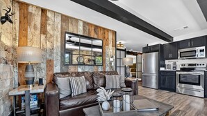 A modern living room with a leather sofa, a coffee table, and a fireplace. The kitchen features stainless steel appliances and dark cabinetry. - Modern Rustic Loft Suite in Downtown Blue Ridge (Blue Ridge)