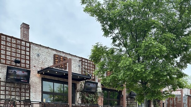 En udendørs terrasse med murstensvægge, udendørs siddepladser og et fjernsyn ophængt på væggen.