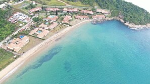 An aerial view of a coastal resort with multiple buildings, a beach, and a clear blue sea. - Cozy beachfront home - 3 suites (Armação dos Búzios)