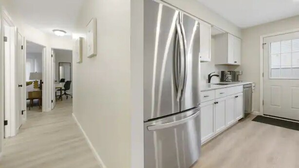 Une cuisine moderne dotée d’appareils électroménagers en acier inoxydable, de meubles blancs et d’un plancher en bois.