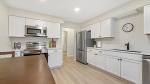 Une cuisine moderne avec des meubles blancs, des appareils en acier inoxydable et une table à manger en bois.