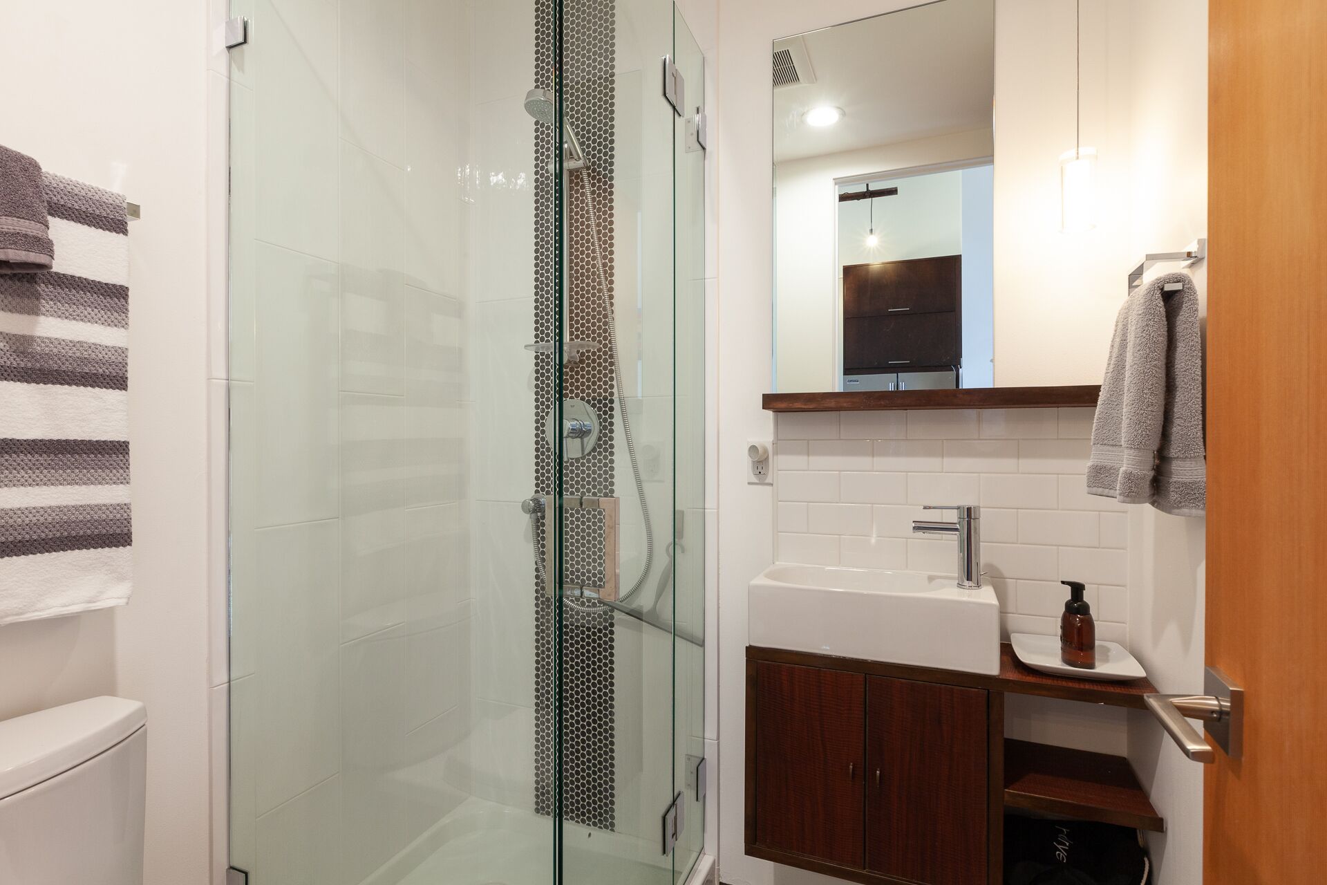Ein modernes Badezimmer mit einer gläsernen Dusche, einem weißen Waschbecken und einem Holzschrank.