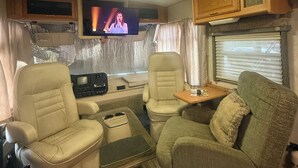 A compact RV interior with a television, seating area, and kitchenette. - Riverside Retreat (Dade City)