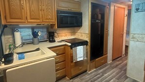 A compact kitchen with wooden cabinets, a microwave, a stove, and a refrigerator. - Riverside Retreat (Dade City)