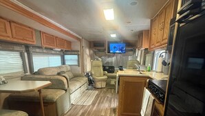 An RV interior with a kitchen, dining area, and a TV mounted on the wall. - Riverside Retreat (Dade City)