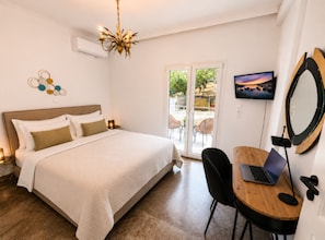 A bedroom with a bed, a desk with a laptop, a TV, and a balcony with chairs.