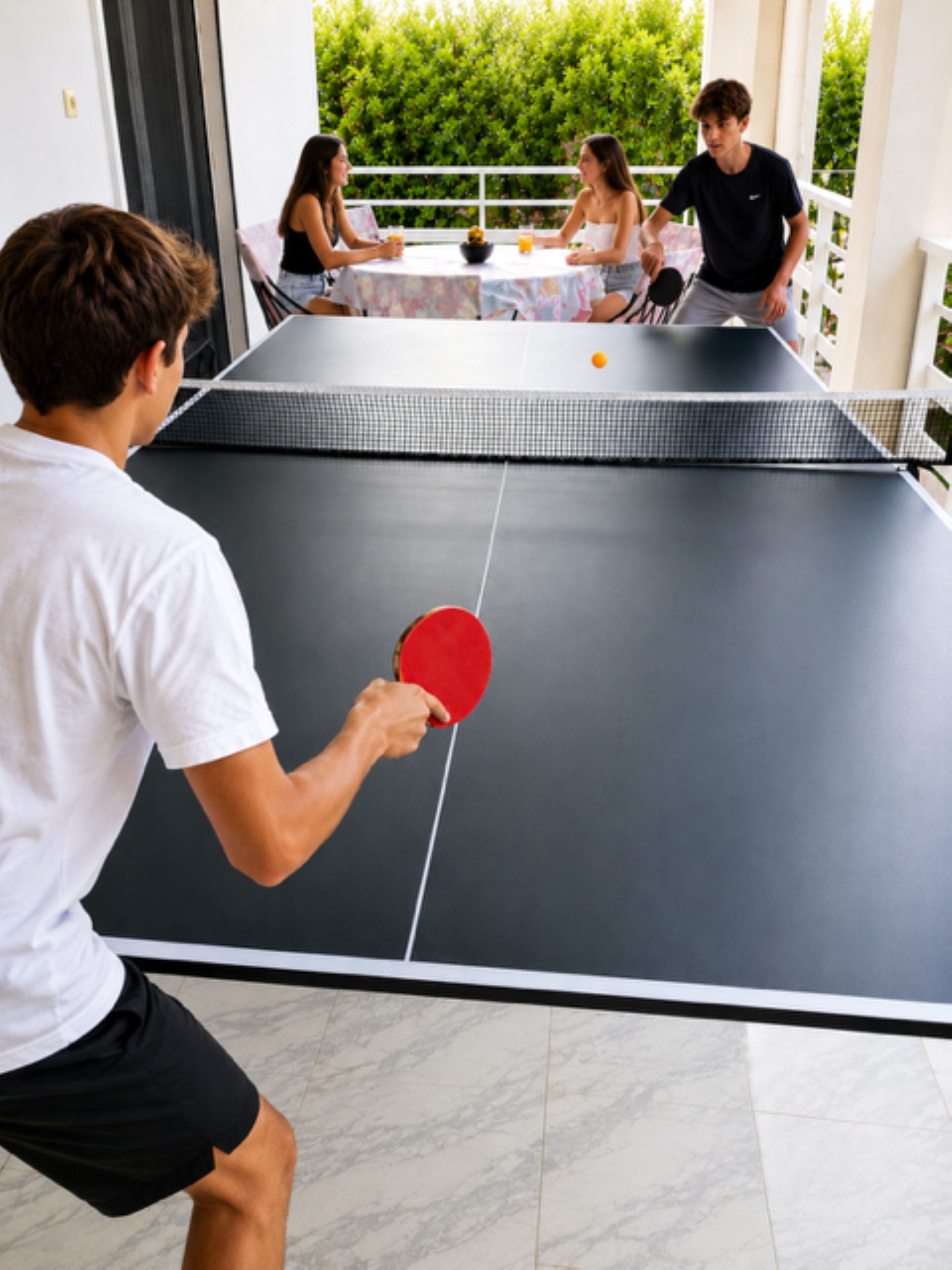 Ein Tischtennis-Tisch mit einer spielenden Person, umgeben von einer Gruppe von Personen, die an einem Tisch sitzen.