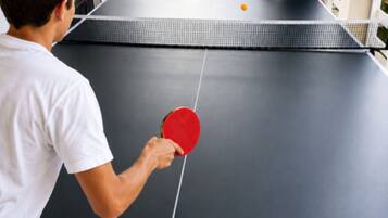 Ein Tischtennis-Tisch mit einer spielenden Person, umgeben von einer Gruppe von Personen, die an einem Tisch sitzen.