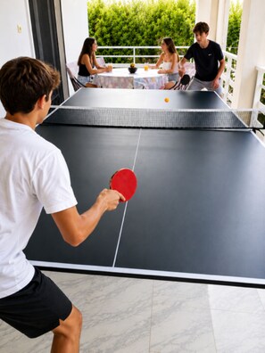 Ein Tischtennis-Tisch mit einer spielenden Person, umgeben von einer Gruppe von Personen, die an einem Tisch sitzen.