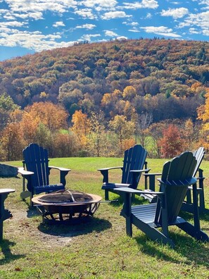Leirintäalue, jossa on Adirondack-tyylisiä puutarhatuoleja ja nuotiopaikka. Alueen ympärillä on nurmikenttä ja puita, joiden lehdet ovat syksyn väreissä.