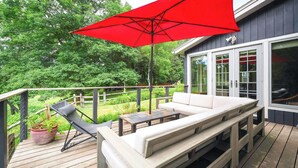 Una terraza de madera con un paraguas rojo, un sofá blanco y una pequeña mesa.