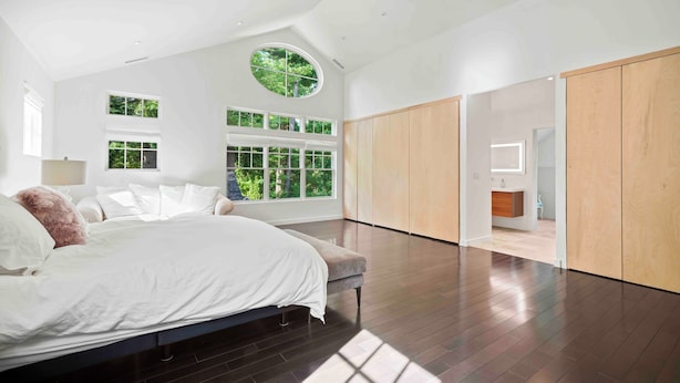 Un dormitorio moderno con una cama grande, un tragaluz circular y vistas al exterior con vegetación.