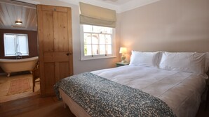A bedroom with a large bed, a wooden door, a window with curtains, a lamp, and a vintage-style bathtub. - 5 East Street  (Rye)