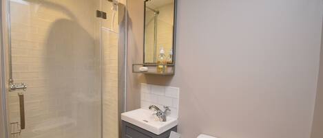 Une salle de bain avec une douche à parois de verre, un lavabo blanc, un miroir et des toilettes.