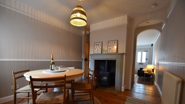 A dining area with a round wooden table, wicker chairs, a chandelier, a fireplace, and a hallway leading to another room. - 5 East Street  (Rye)