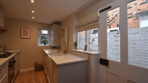 A compact kitchen with white cabinetry, a built-in sink, and a window with a view of a brick wall. - 5 East Street  (Rye)