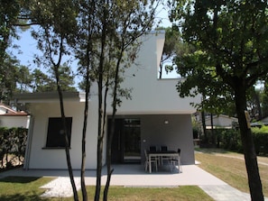 A modern two-story house with a patio, a dining table, and chairs.