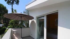 A balcony with a table and chair, a patio umbrella, and a sliding glass door leading to an interior room. - Tranquil villa in Lignano Pineda (Lignano Sabbiadoro)
