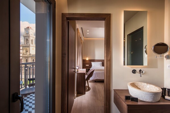 Ein Hotelzimmer mit einem Bett, einem Holztisch, einem runden Spiegel und einem großen Fenster mit Blick auf ein Gebäude.