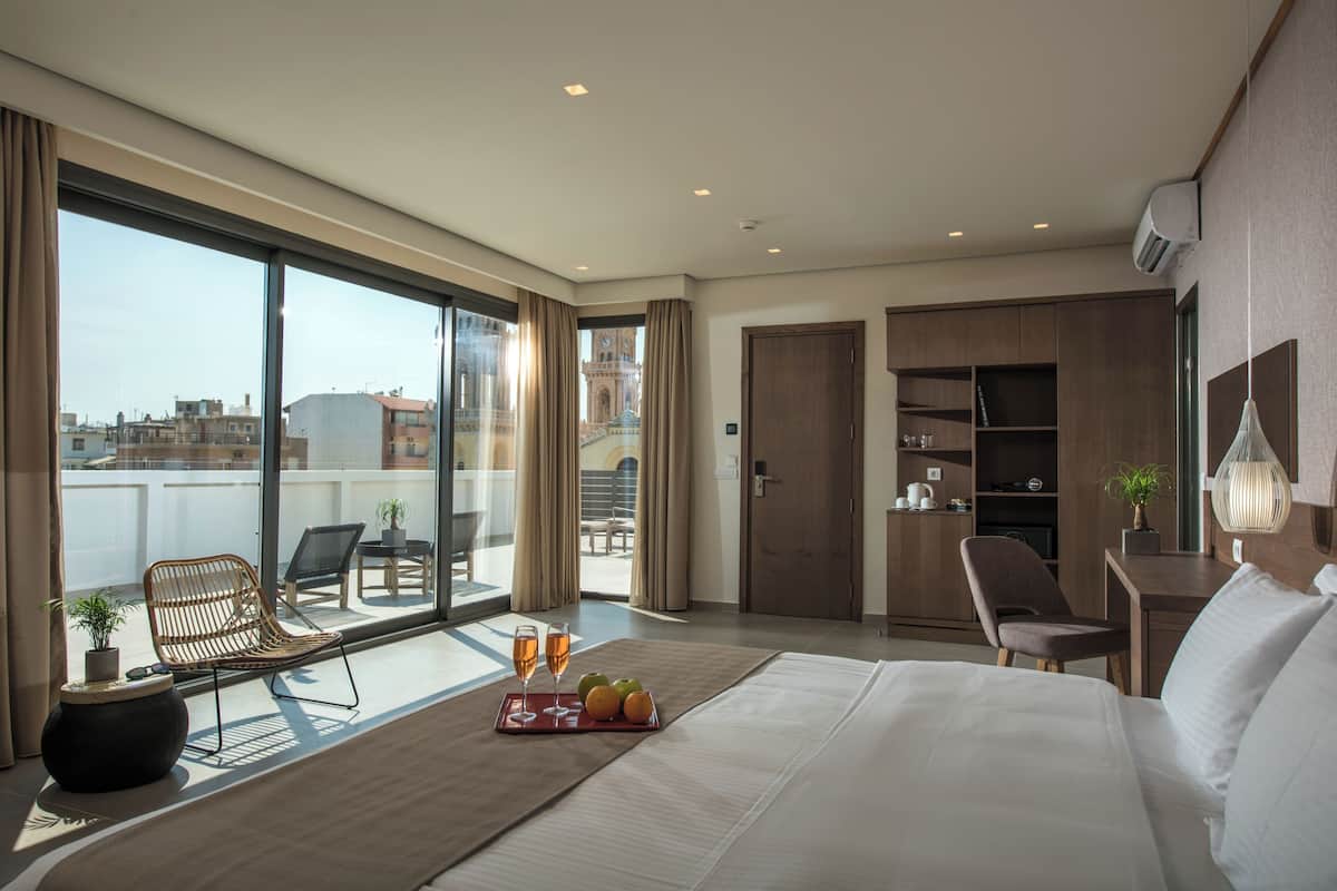 Une chambre d’hôtel moderne dotée d’un grand lit, d’un balcon avec coin salon et offrant une vue sur le paysage urbain.