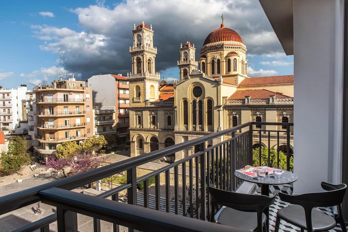 Un balcon avec une table et des chaises, donnant sur un paysage urbain avec des bâtiments historiques et un ciel dégagé.