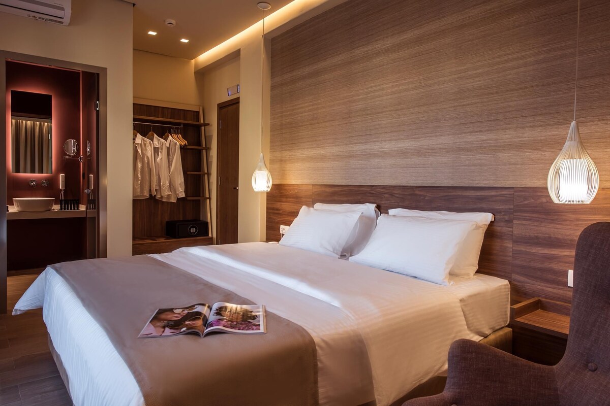 Habitación de hotel con una cama, un armario, una tocador con espejo y una lámpara colgante.
