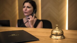 Un comptoir d’accueil d’hôtel avec un classeur noir et une clochette métallique.