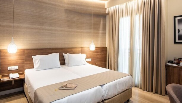 Une chambre d’hôtel avec un grand lit, une tête de lit en bois, deux lampes de chevet et une fenêtre avec des rideaux.