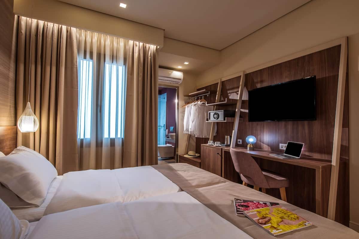 Une chambre d’hôtel avec deux lits, un bureau avec un ordinateur portable, une télévision et une armoire.