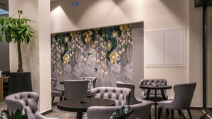 Un espace de détente moderne avec des fauteuils capitonnés, une table ronde et une grande fresque murale abstraite.