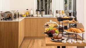 Un buffet de petit-déjeuner proposant une variété d’aliments et de boissons, une machine à café et un panier de fruits.